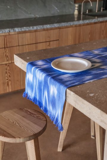 Camino de mesa artesanal en tonos azules con tejido mallorquín de Teixits Vicens sobre mesa rústica
