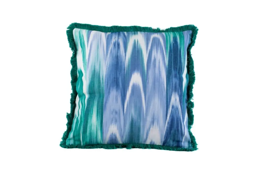 Cojín decorativo con flecos verdes y diseño de rayas ikat en tonos azules, turquesa y blanco