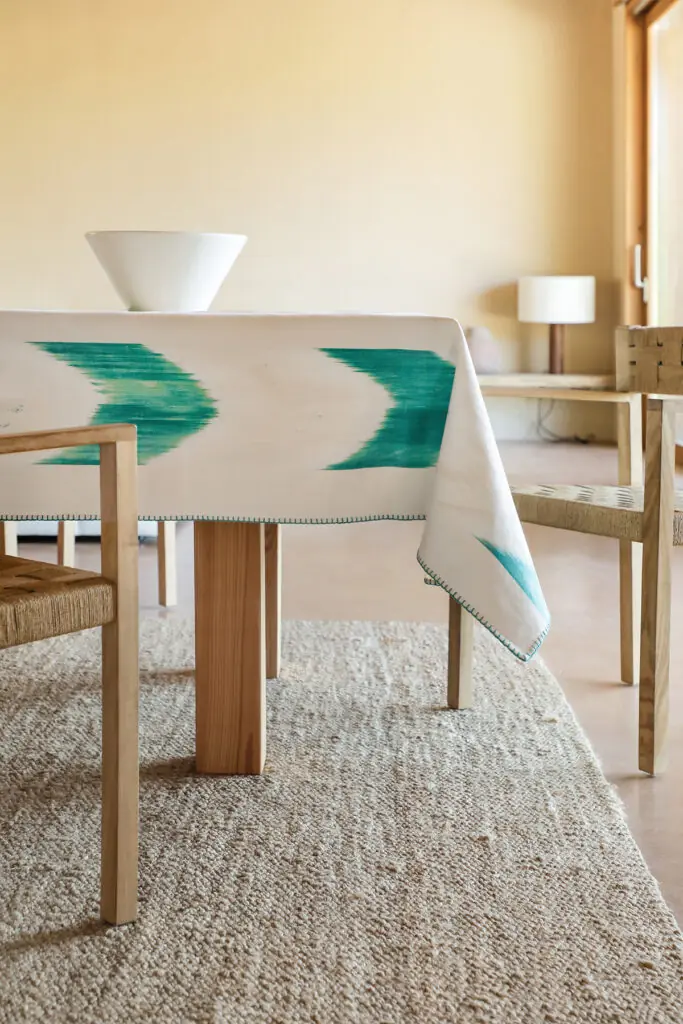 Mantel blanco con estampado ikat en verde turquesa colocado en una mesa de comedor de madera clara
